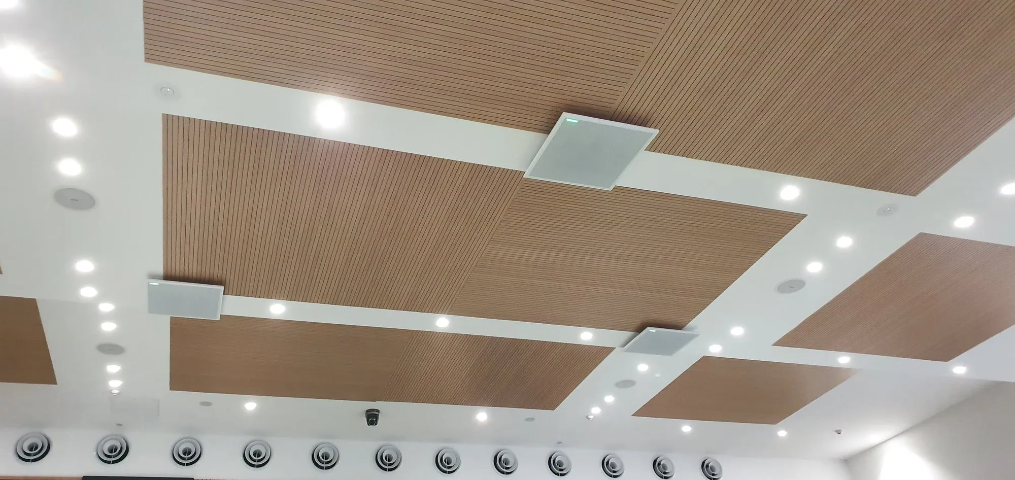 Looking up at an array of timber acoustic ceiling rafts with flush ceiling speakers between them