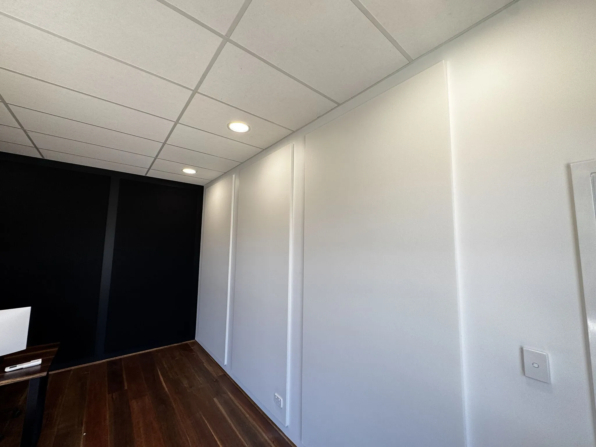 Fabric-wrapped acoustic wall panels installed floor to ceiling alongside a dark feature wall
