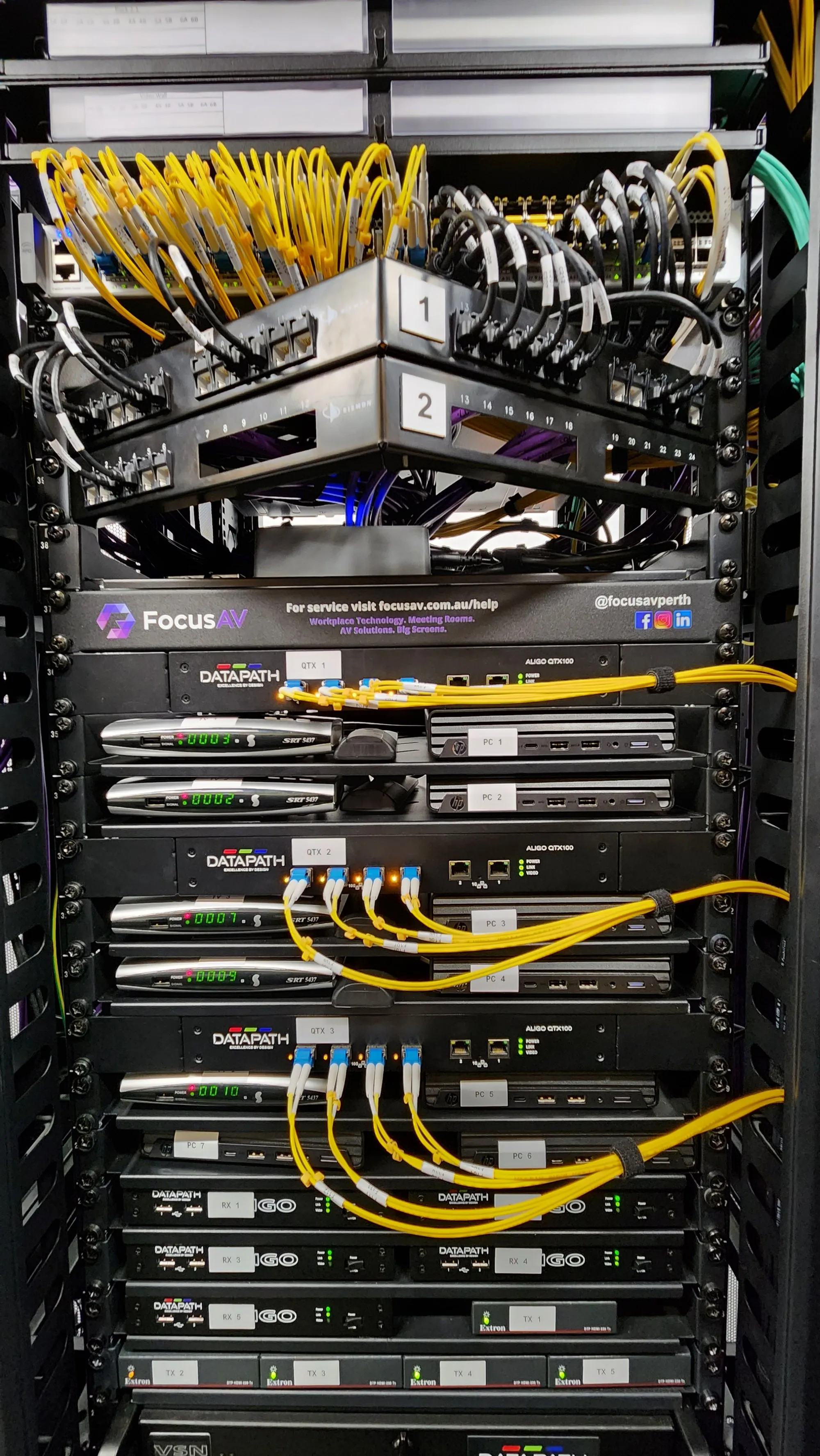 An AV rack with yellow patch leads, powered devices and status lights