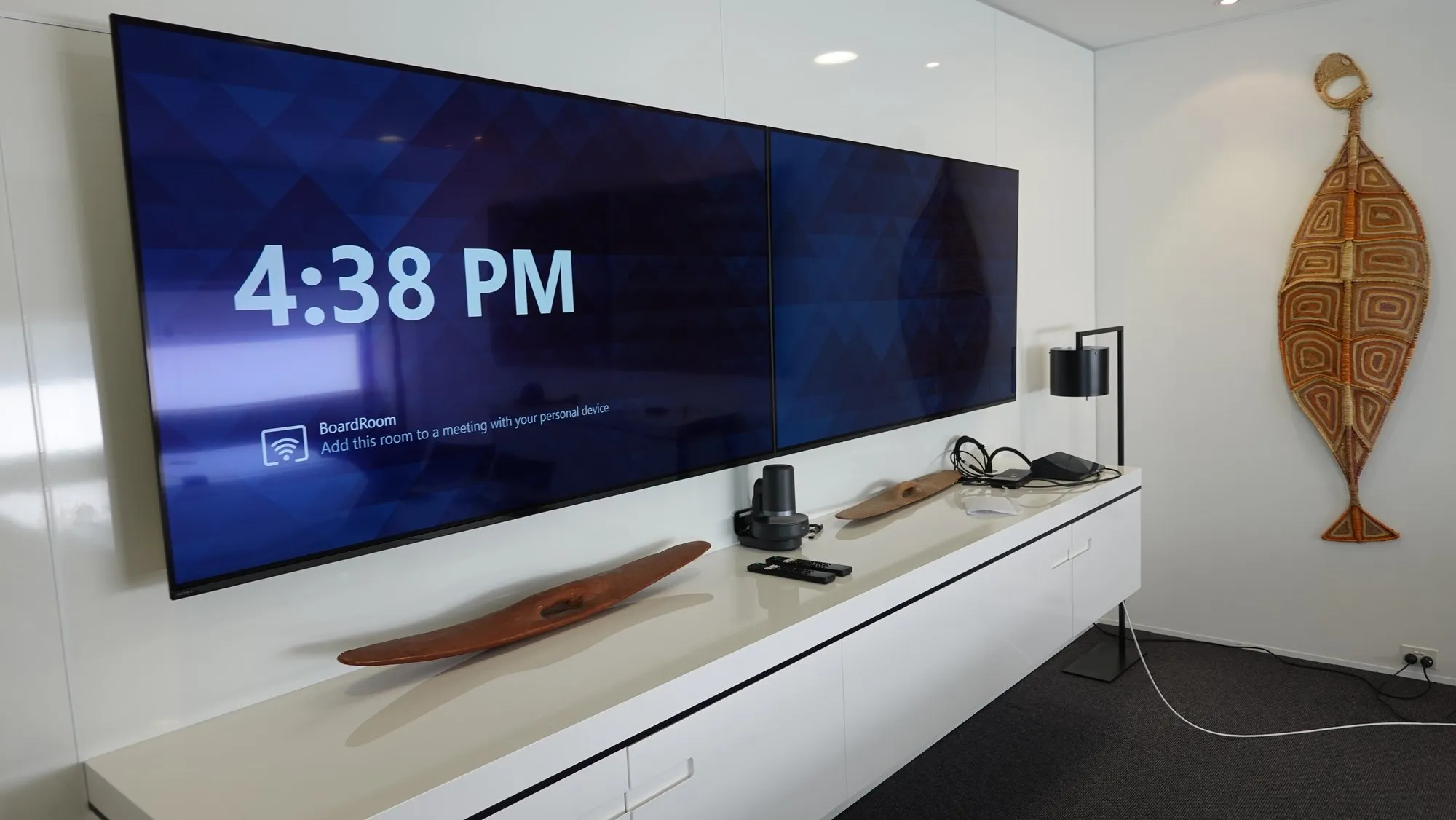 Dual displays above a low white credenza with BYOD connectivity on top, artwork alongside