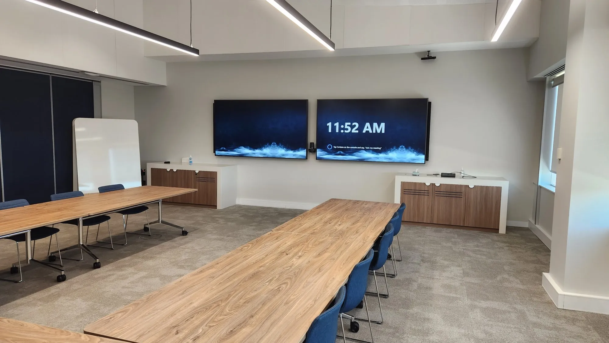 A long boardroom with a timber table, dual displays and a whiteboard alongside