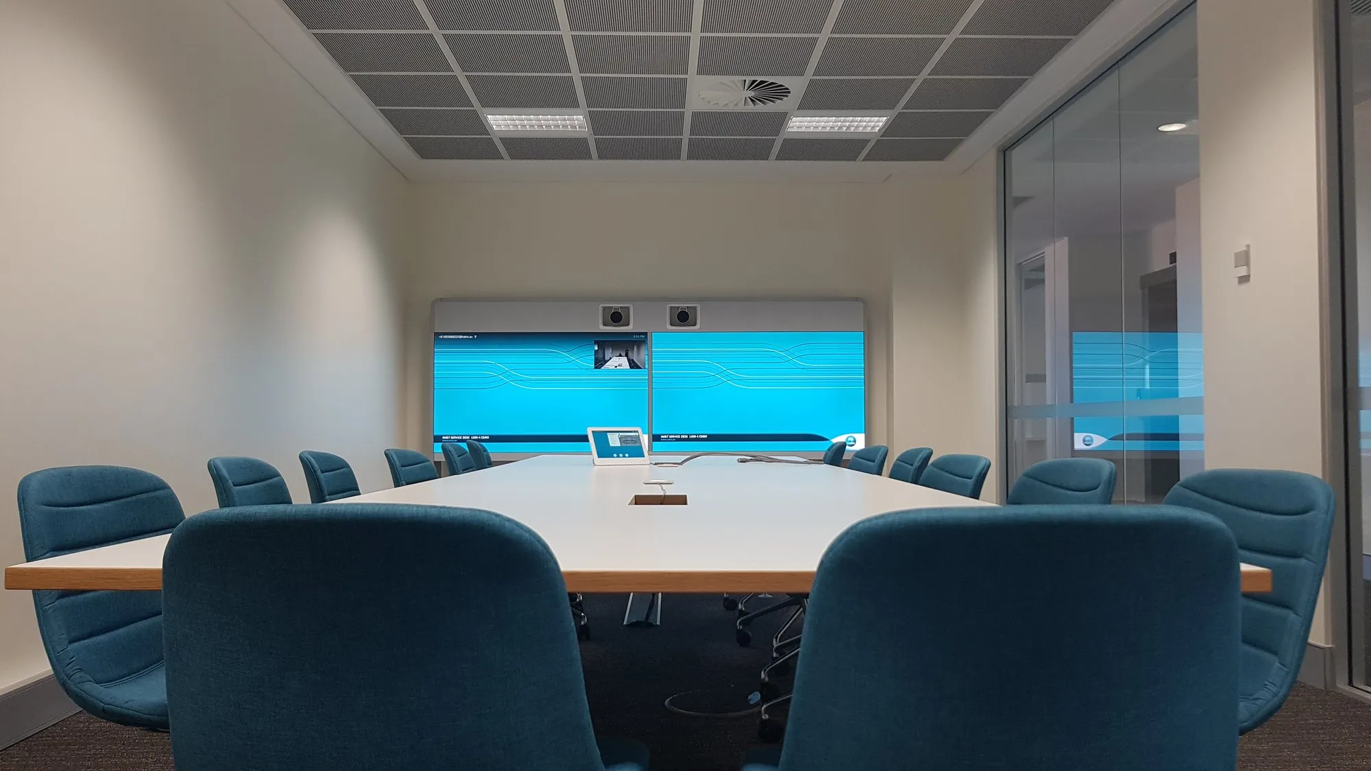 A boardroom with teal chairs and dual displays on the end wall