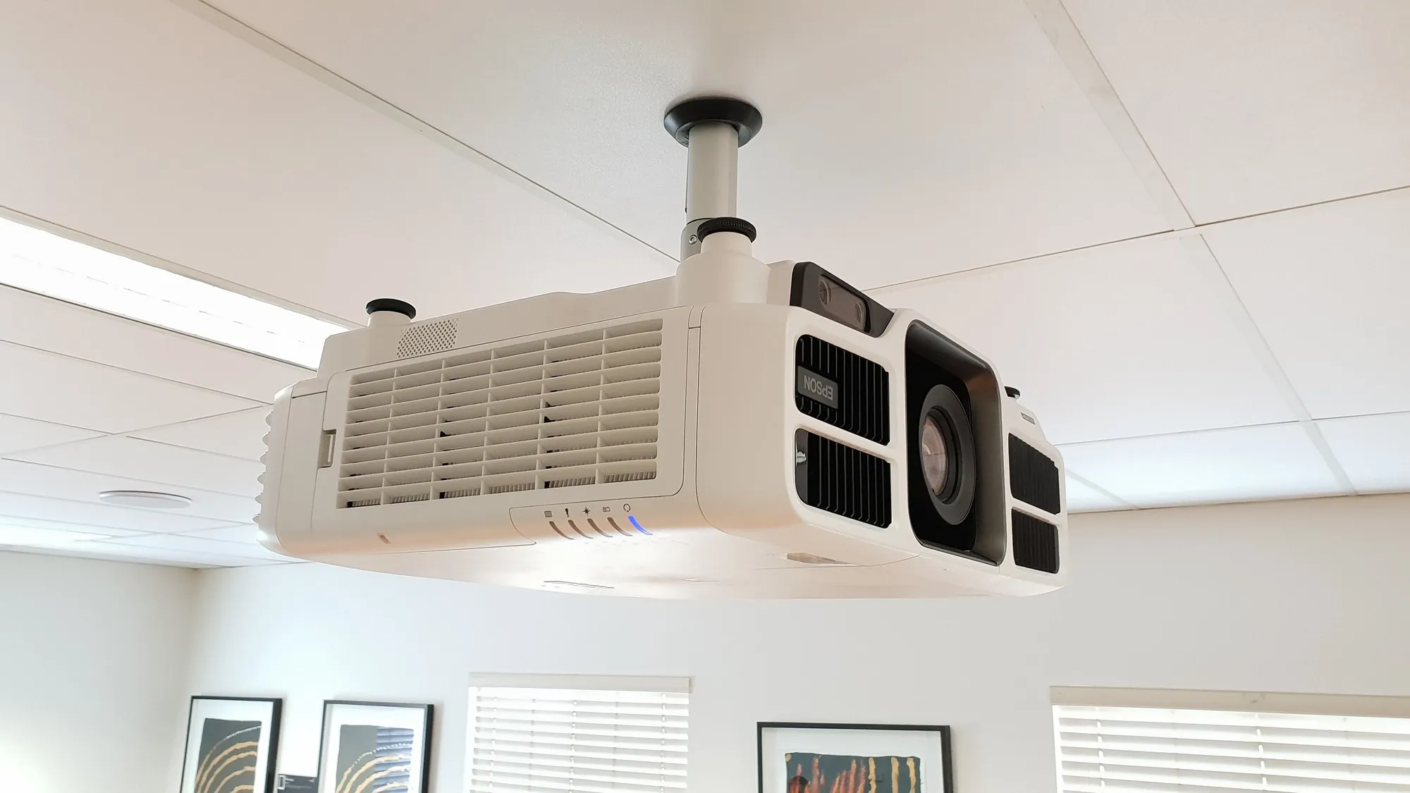 A ceiling-mounted projector fitted into a suspended ceiling grid