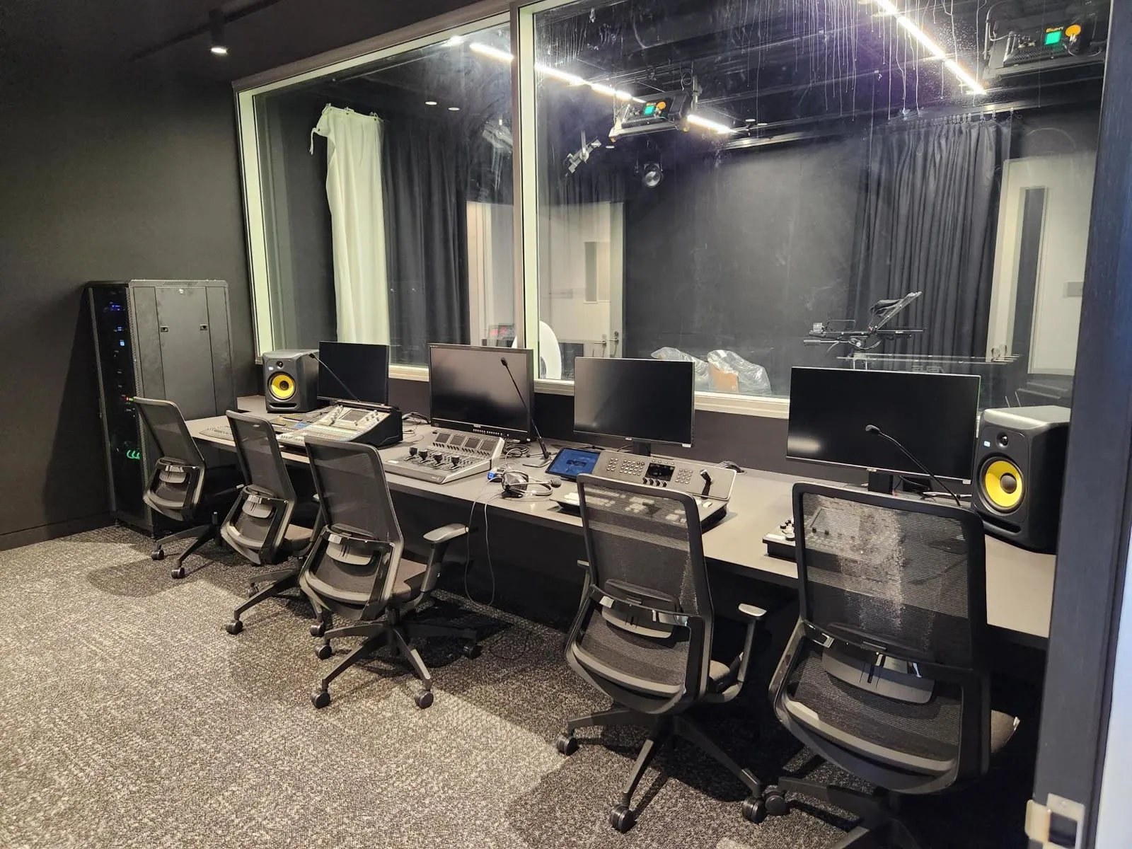 The control room of Hale School's media studio — mixing desks, studio monitors and a glass window into the blacked-out studio floor