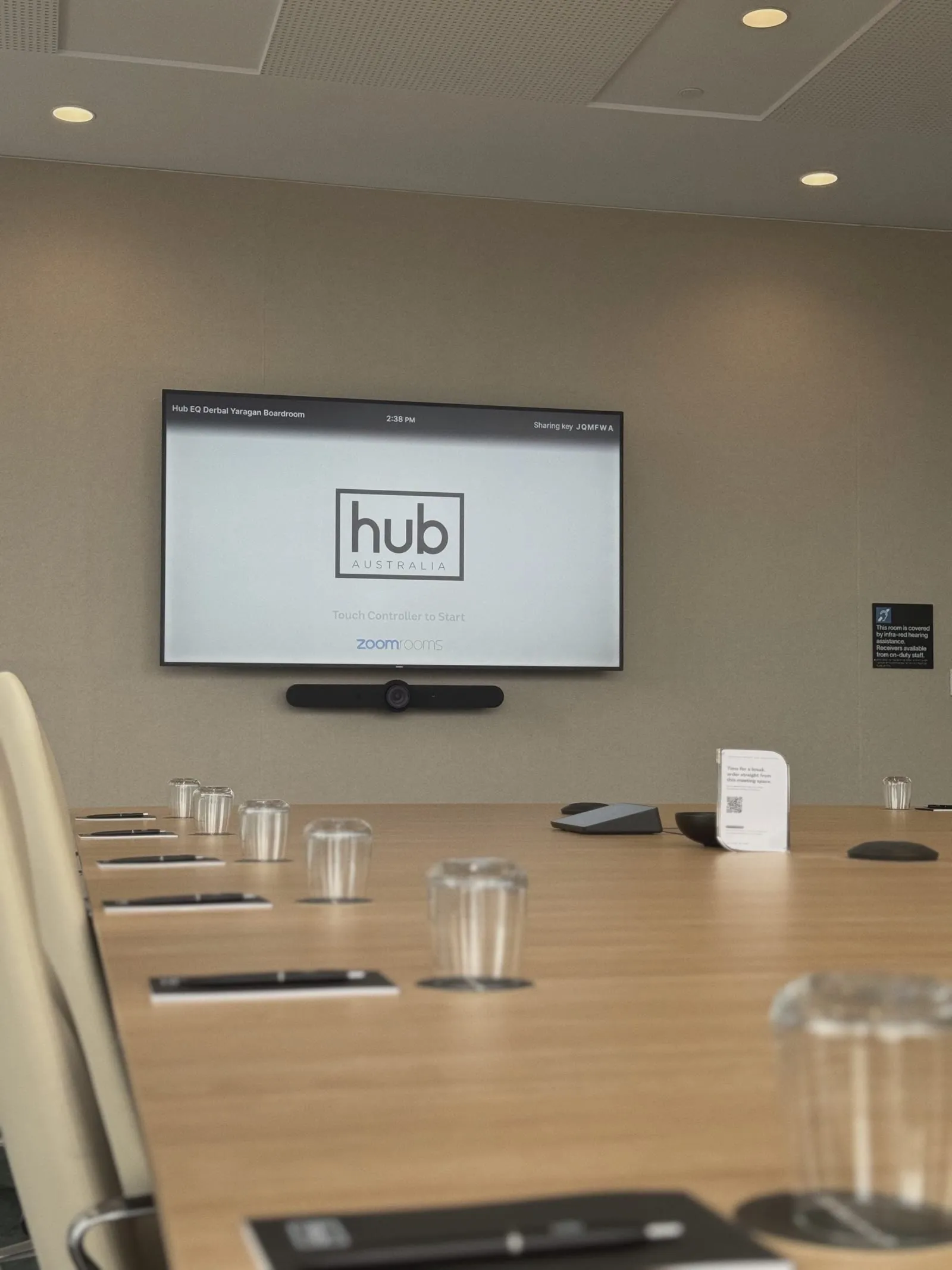 Hub Australia's boardroom at Nine The Esplanade, Perth — a wall display showing the room's booking screen, a certified video bar mounted beneath it and a touch controller on the long timber boardroom table
