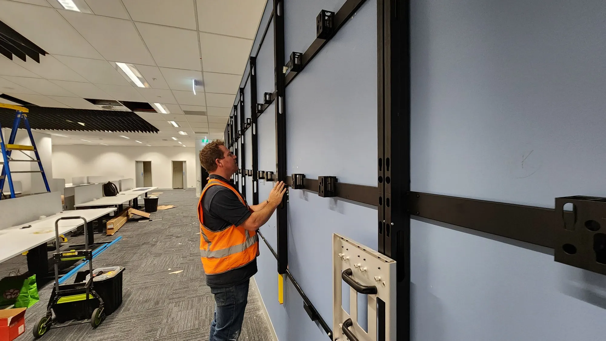 An installer in hi-vis working at a wall frame in an unfinished commercial space