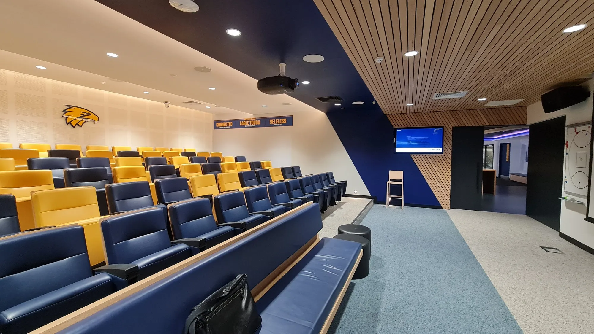 A tiered theatrette with banked navy-and-gold seating facing the presentation wall