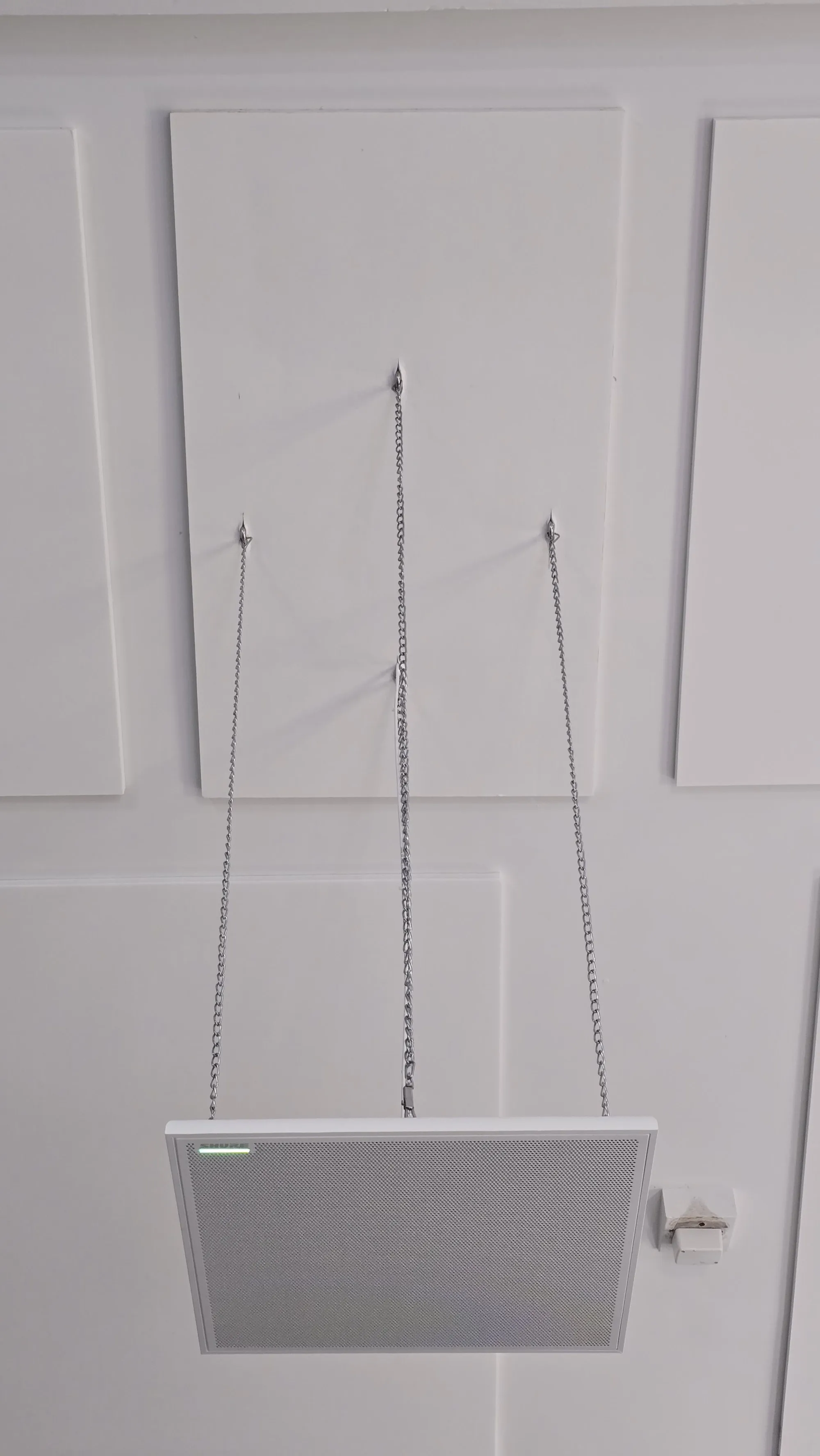 A suspended acoustic raft hanging on its chains against a wall of flush acoustic panels, part-way through the Lihir install