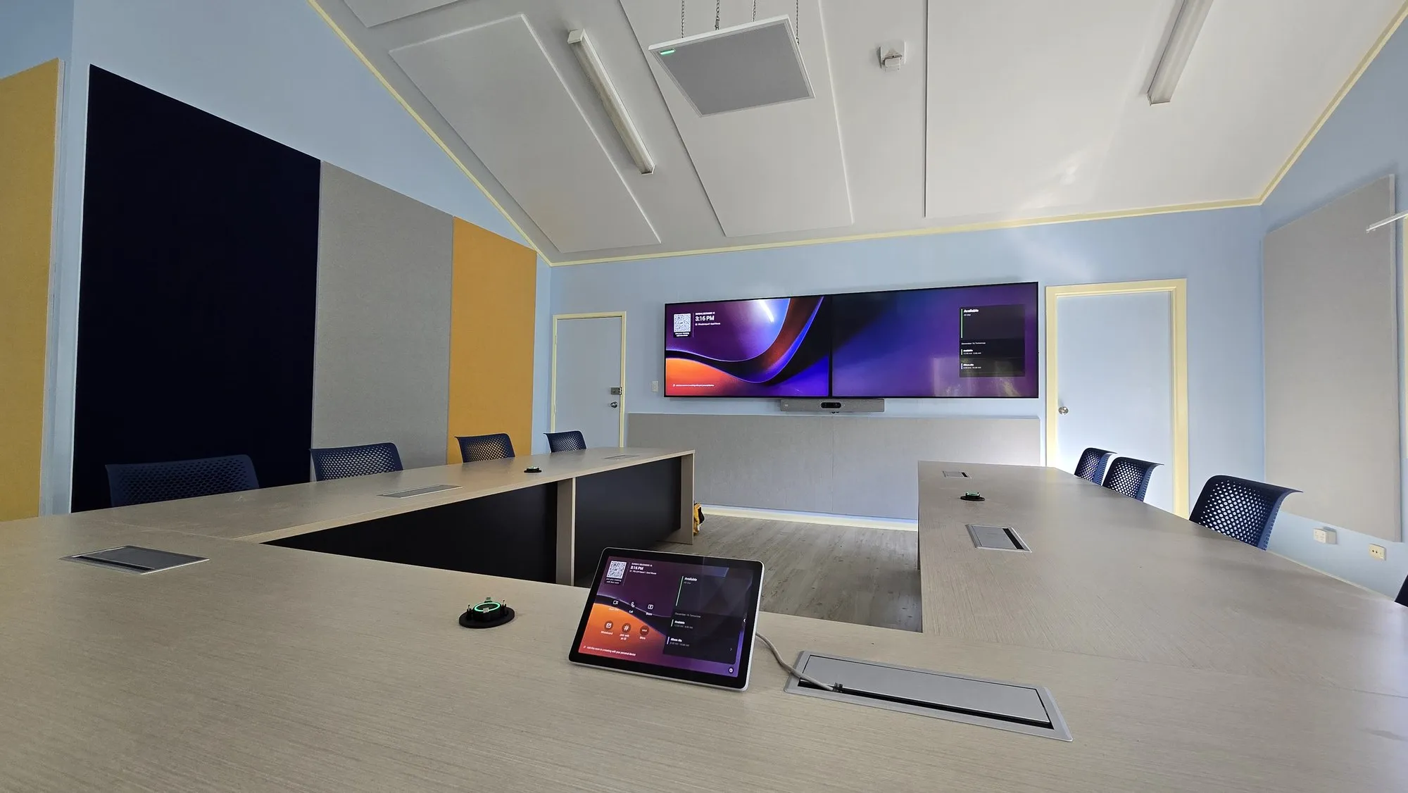 A touch controller on a conference table with the widescreen display beyond