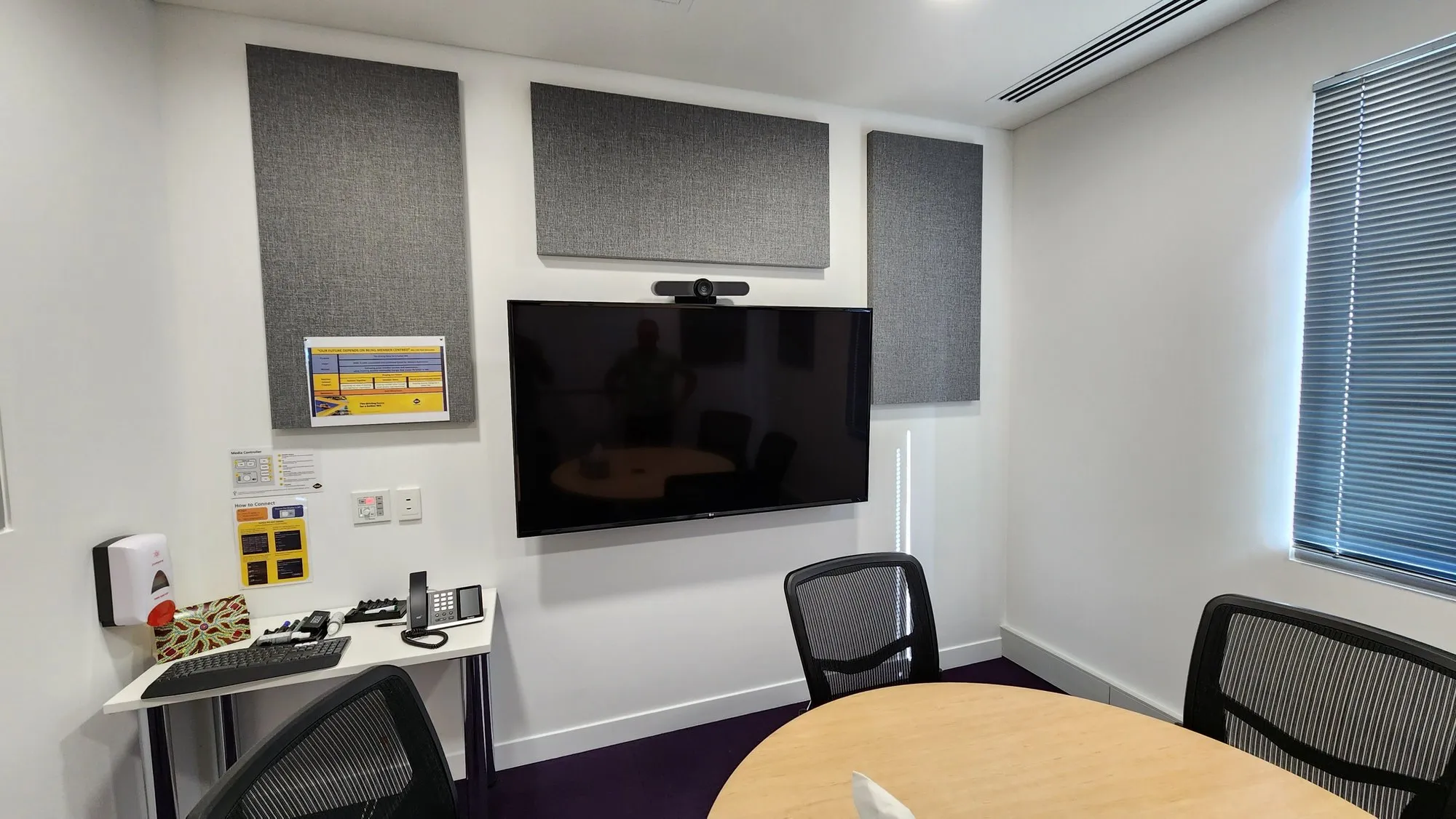 A small Perth meeting room with fabric acoustic panels flanking the display wall, camera mounted above the screen