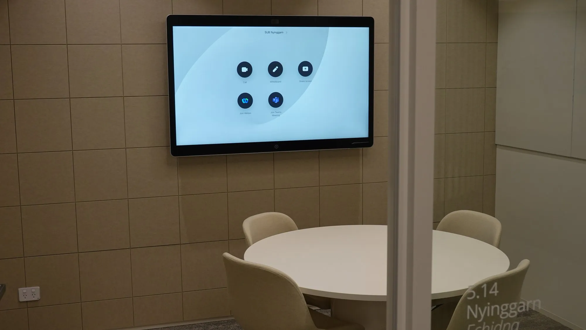 A small huddle room with a wall-mounted touch display showing call and share buttons over a round table