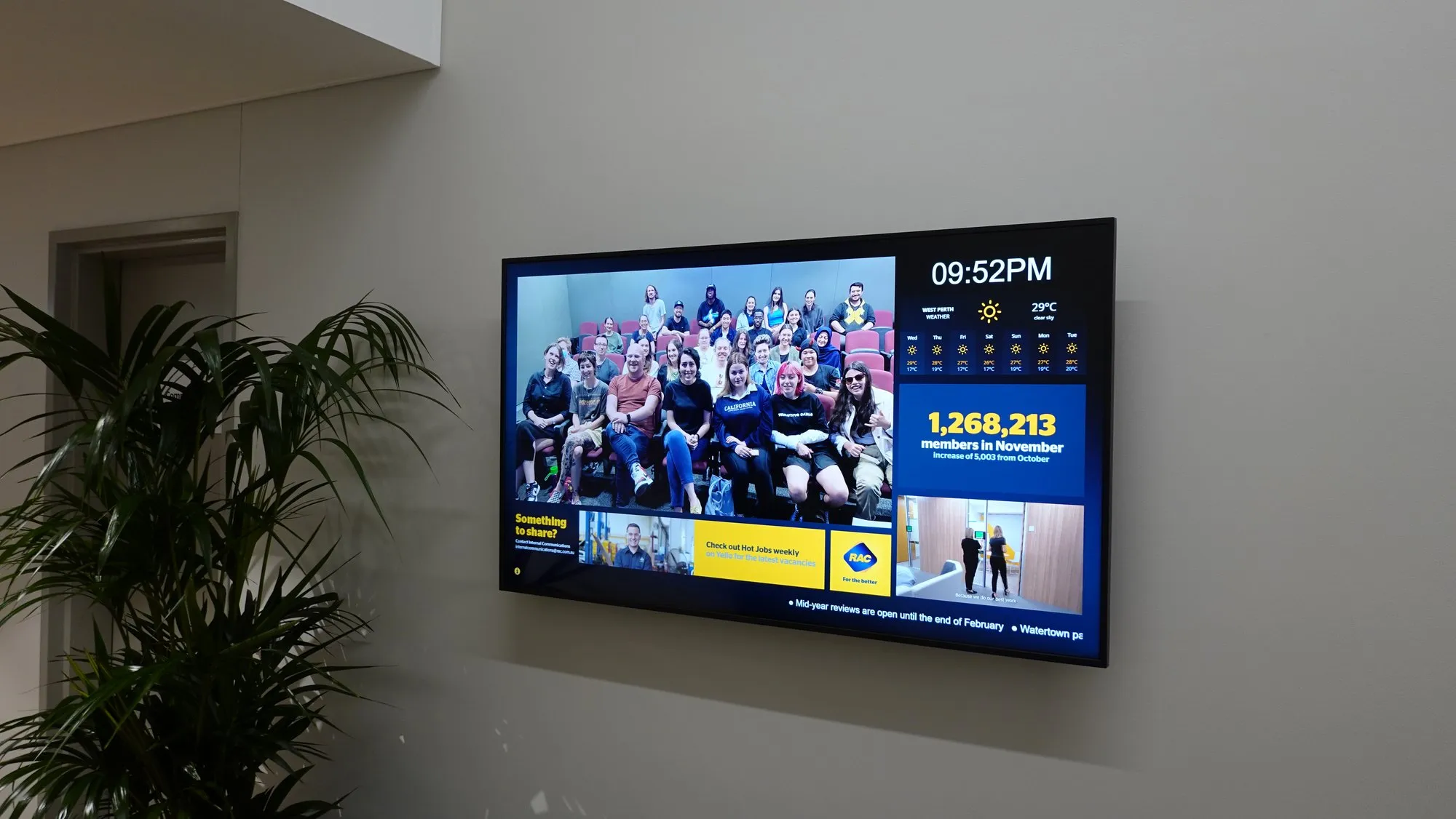 An RAC workplace display running scheduled campaign content beside a live member counter — platform-driven, not USB-fed