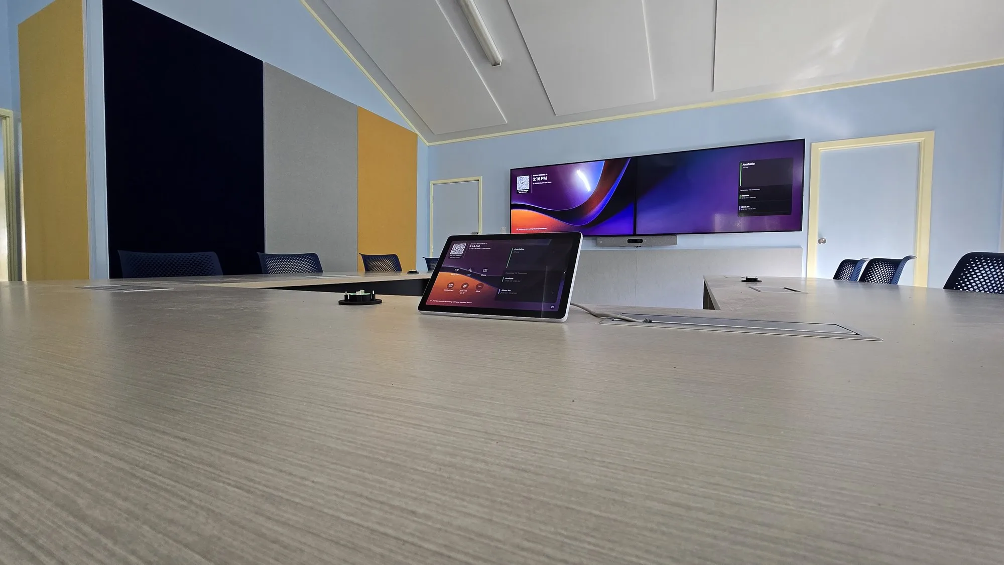 A conference room set up for Teams: U-shaped table run, dual widescreen displays and a video bar on the front wall
