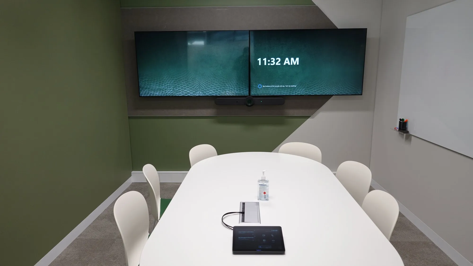 A boardroom table with the touch controller and cable access set into the surface, the display and room panel behind
