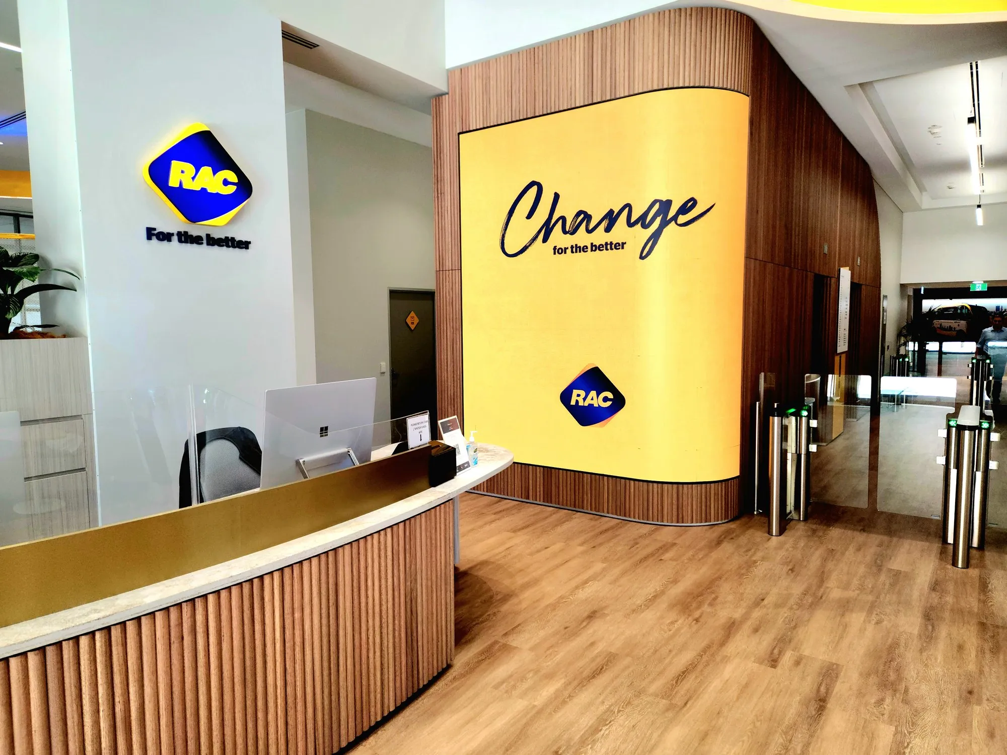 RAC's reception — a curved timber counter beneath the giant yellow Change for the better feature wall