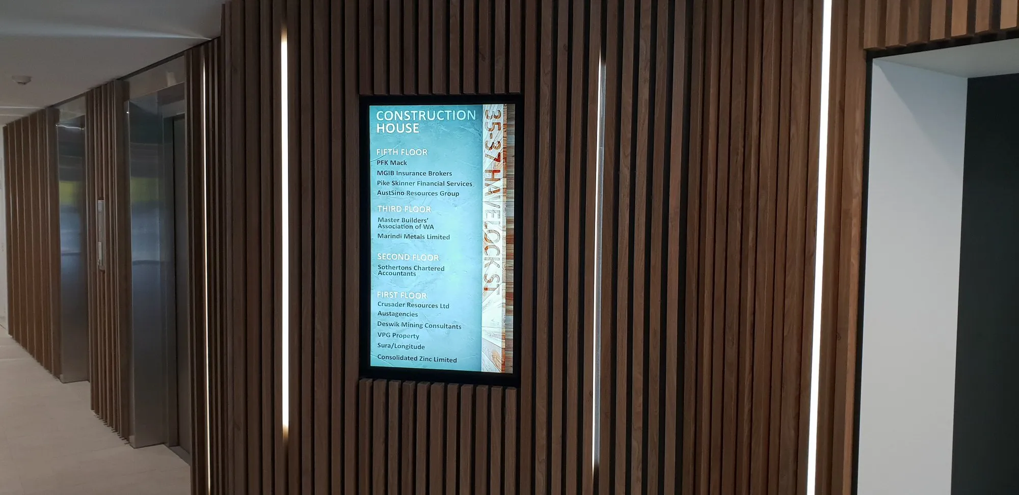 A portrait signage screen recessed flush into a timber batten wall in a corridor