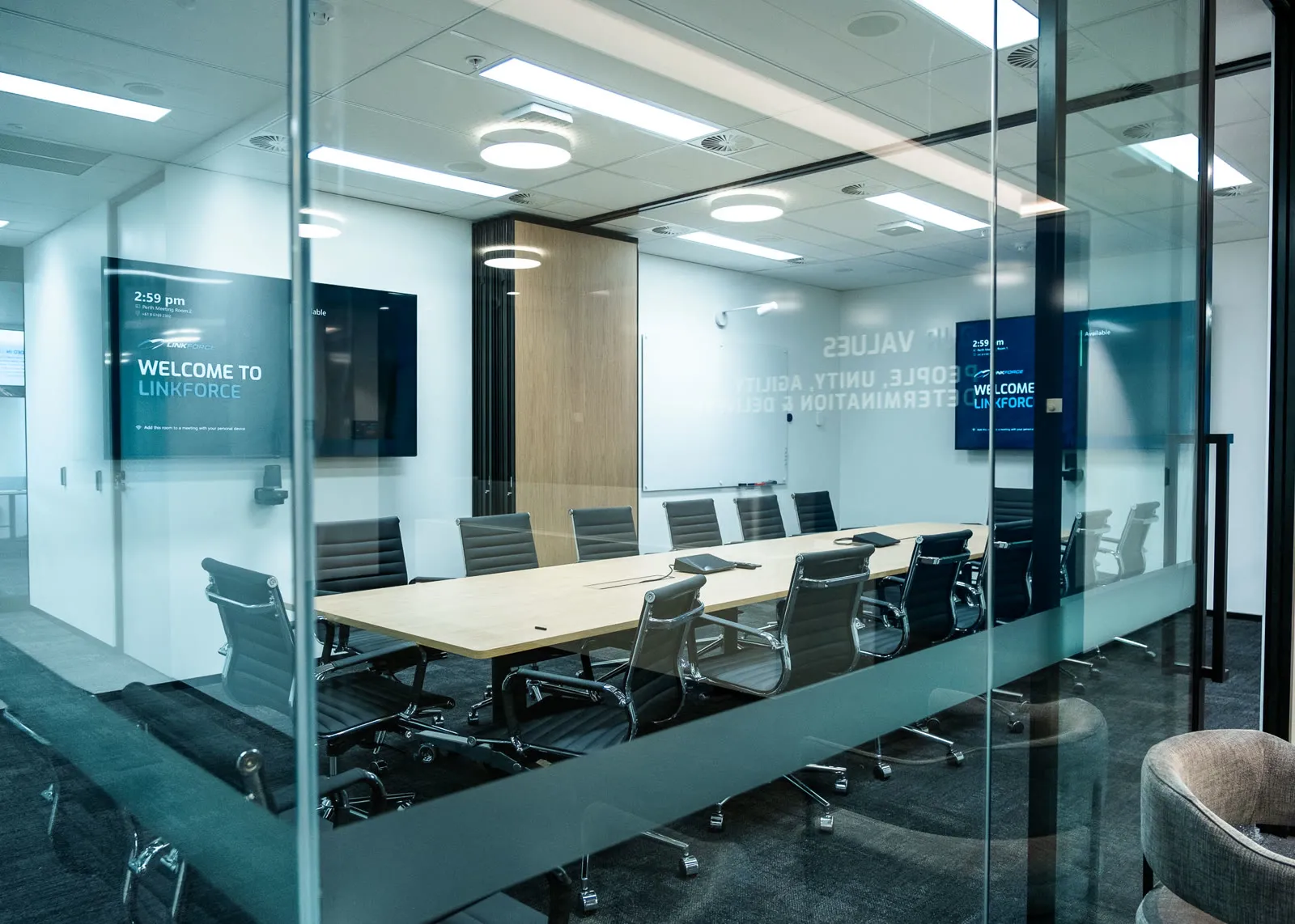 A Linkforce meeting room seen through its glass wall, both displays carrying the branded welcome screen