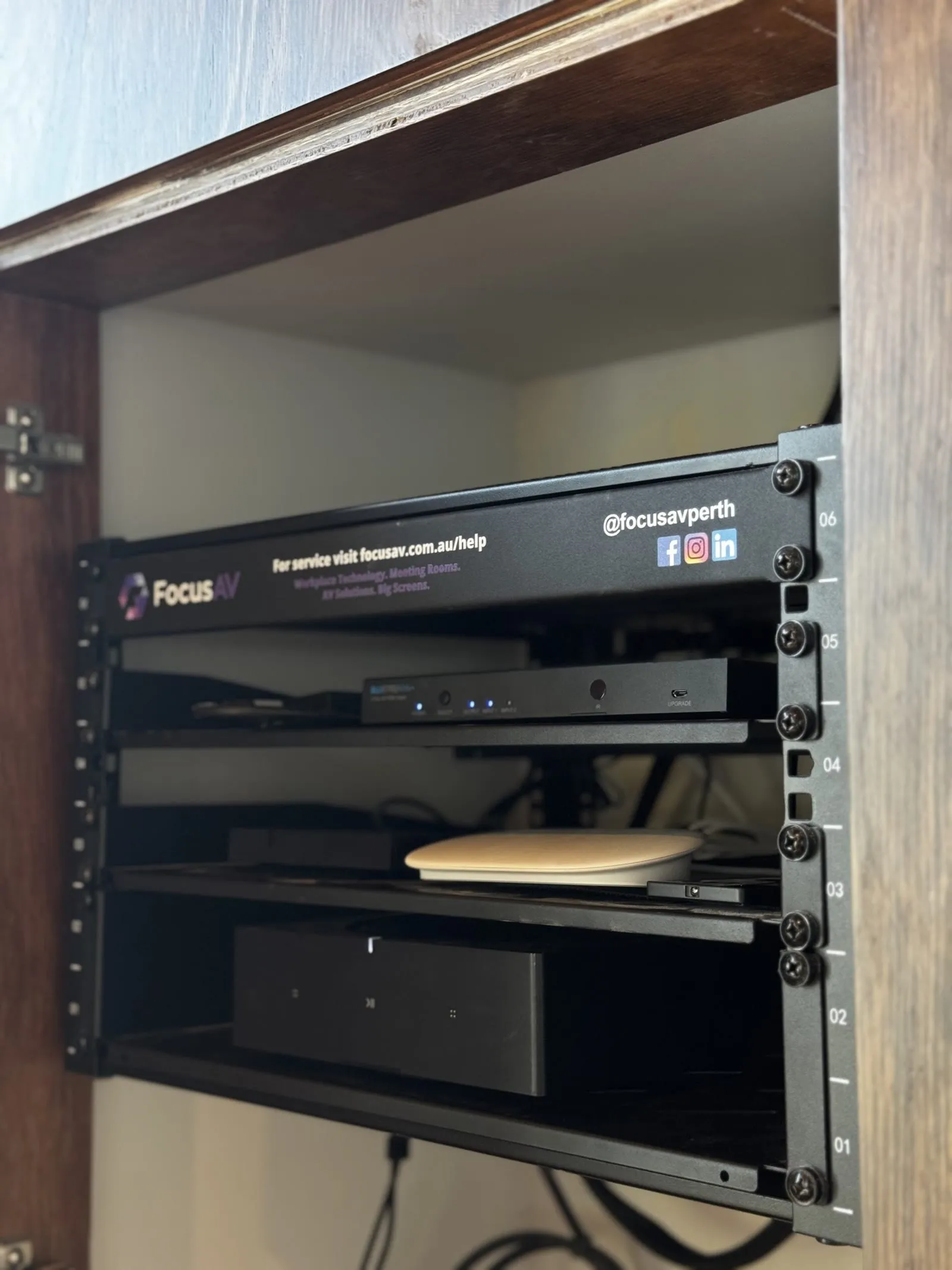 A Focus AV branded equipment rack inside a joinery cabinet, holding the players and switching that drive a building's screens