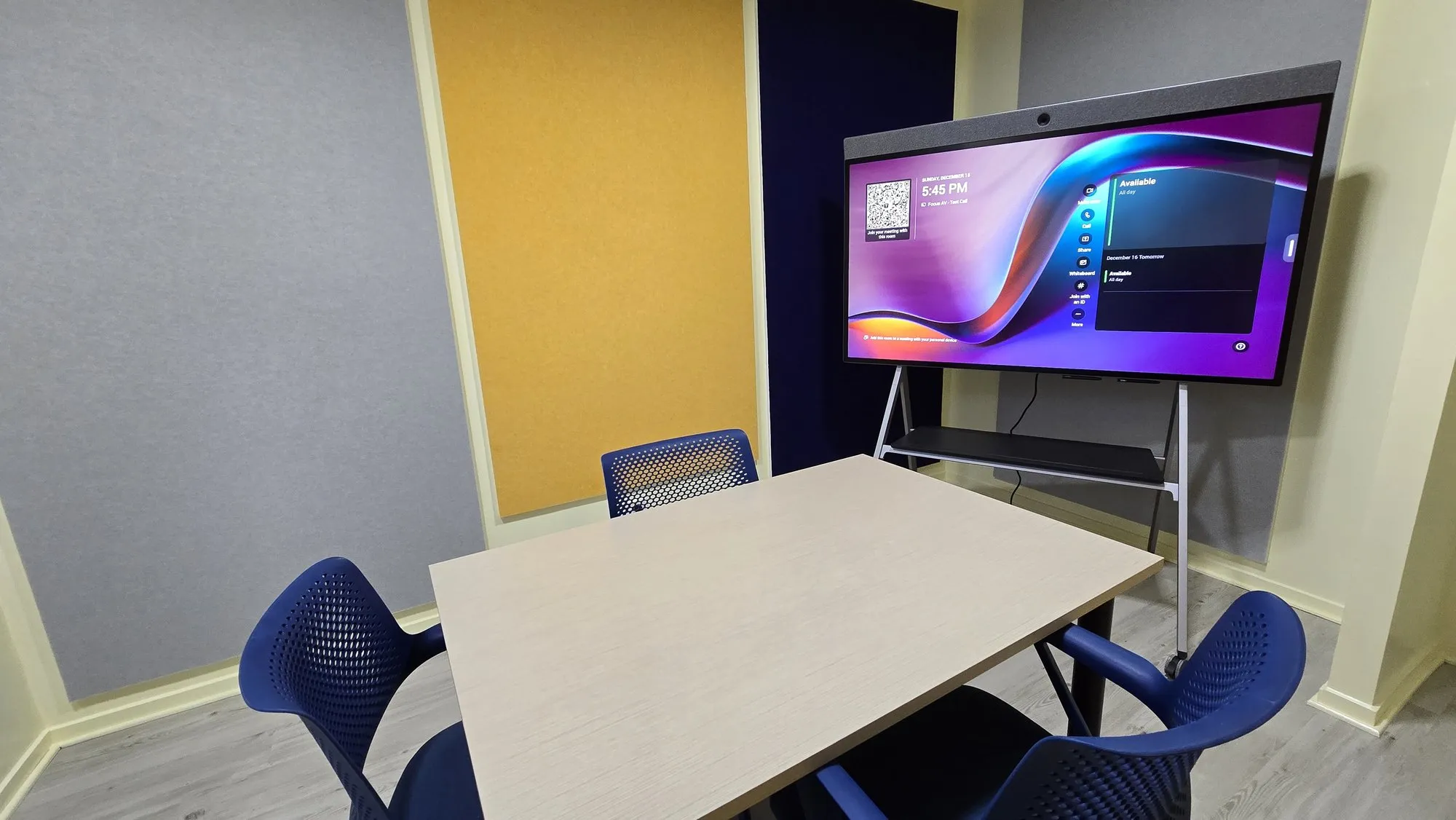 A small room with fabric acoustic panels on the walls and a display on a mobile stand