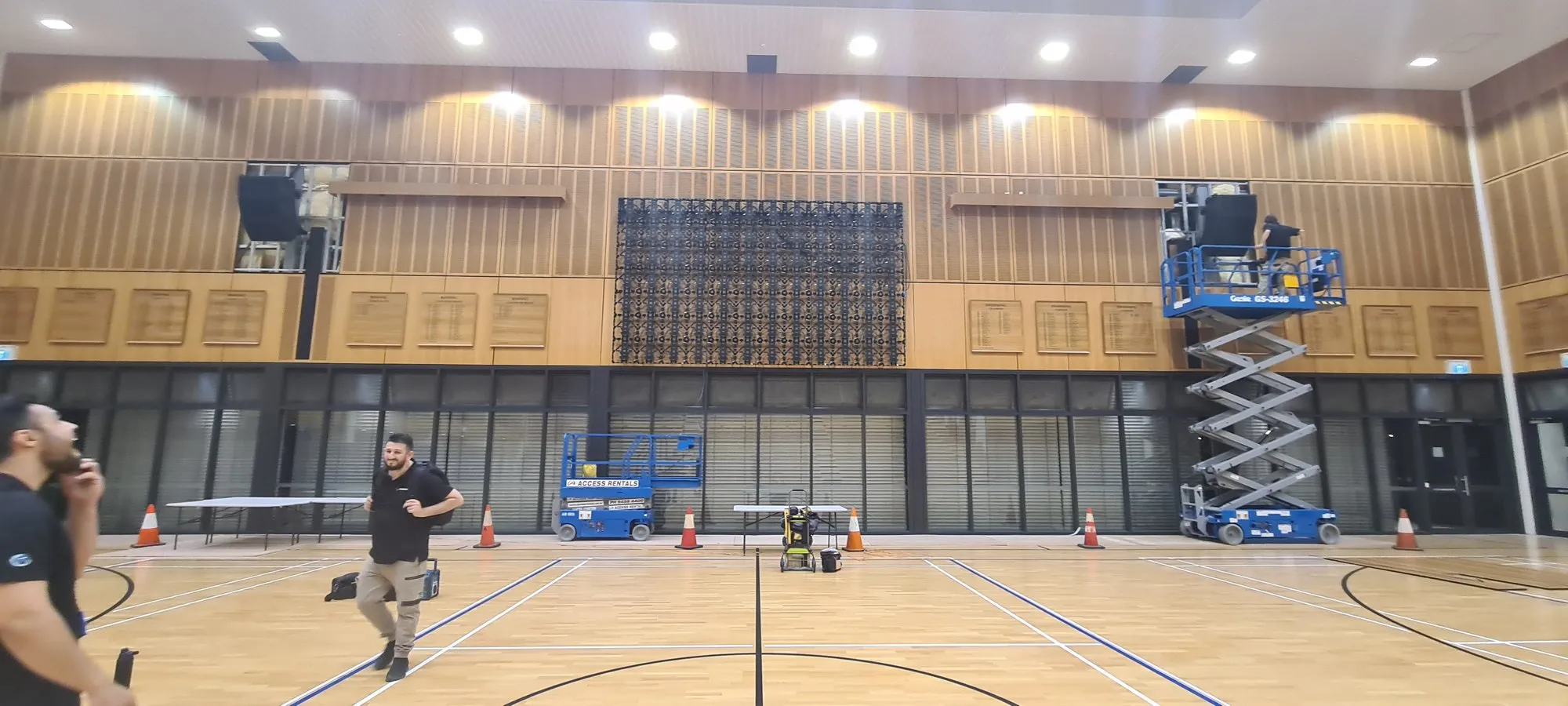 An indoor sports hall with LED panels laid out across the court and scissor lifts in position