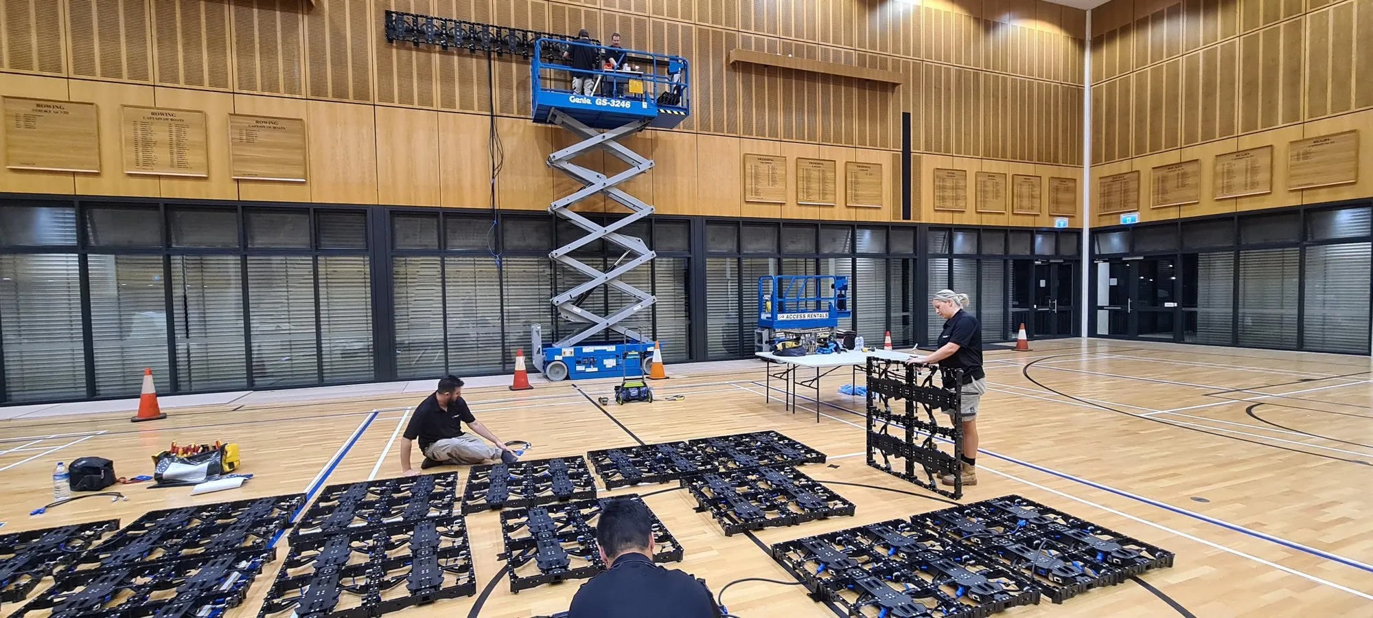 LED cabinets laid out in a grid across a sports hall floor with scissor lifts in position
