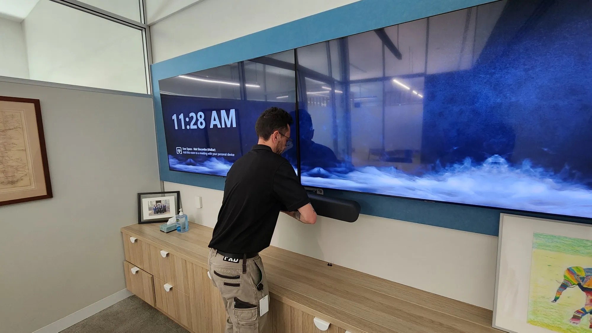 A technician aligning a video bar beneath a wide wall display