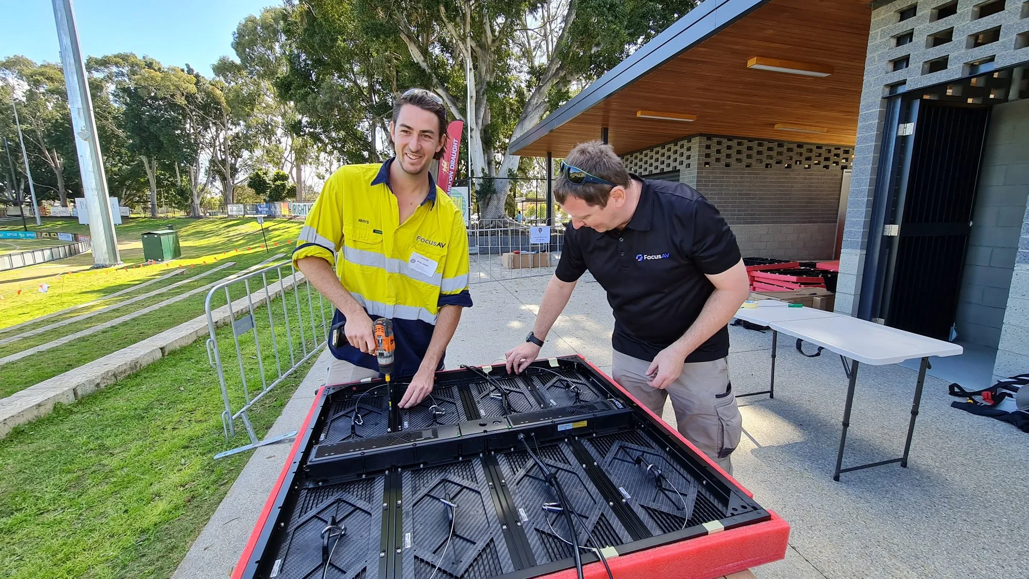 Two technicians assembling LED panels on trestle tables outside a clubroom