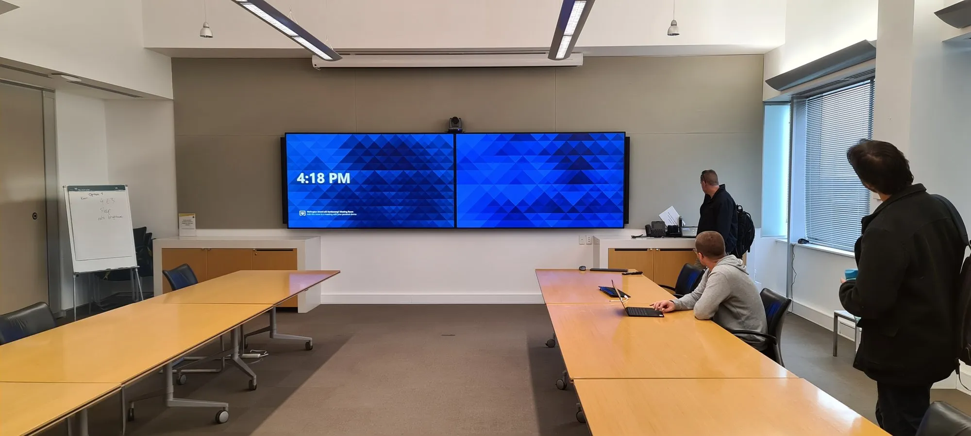 A training room in use with people seated at timber tables facing dual displays