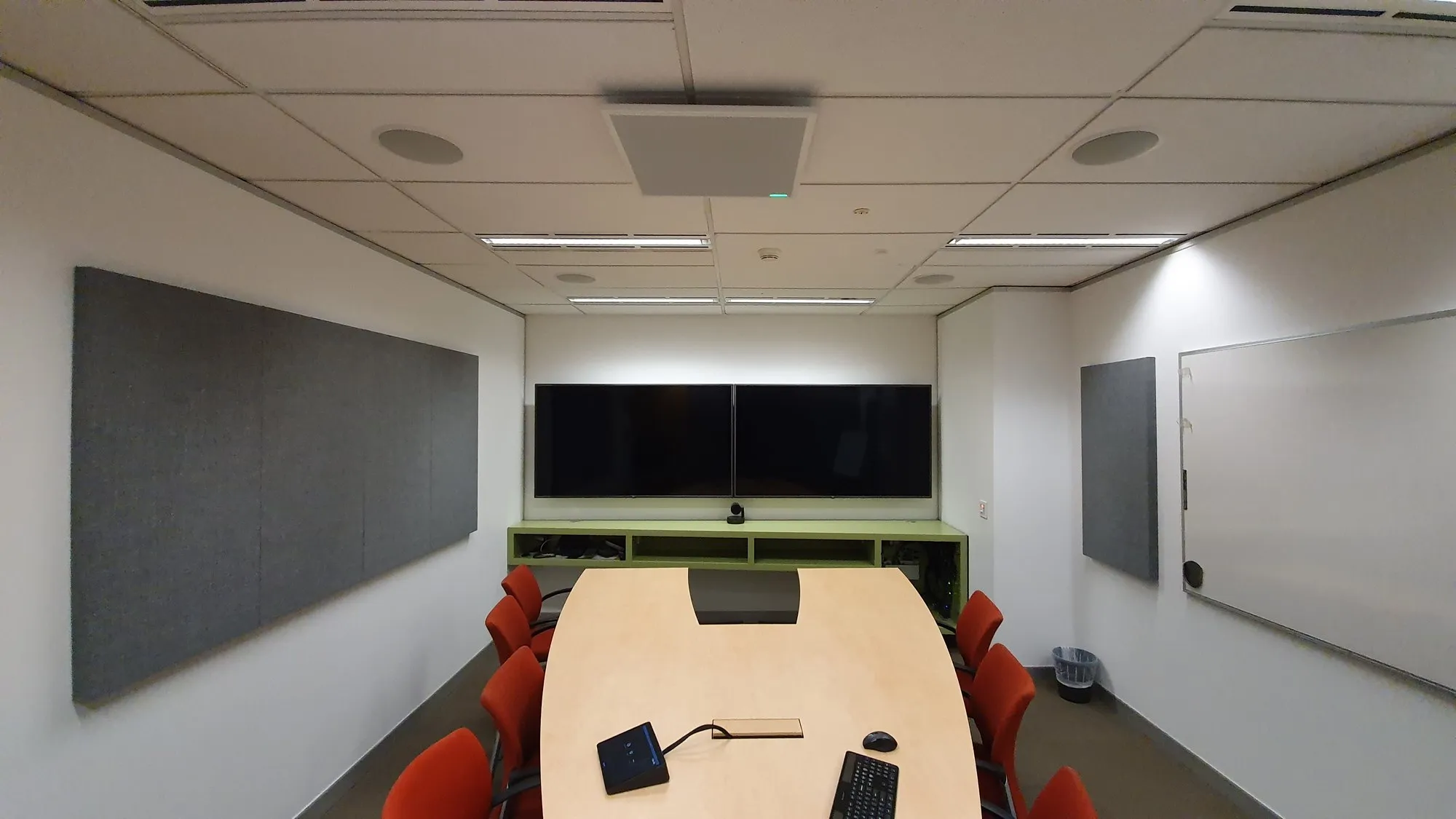 A video-conference boardroom with large grey acoustic panels down both walls, dual displays and a table microphone