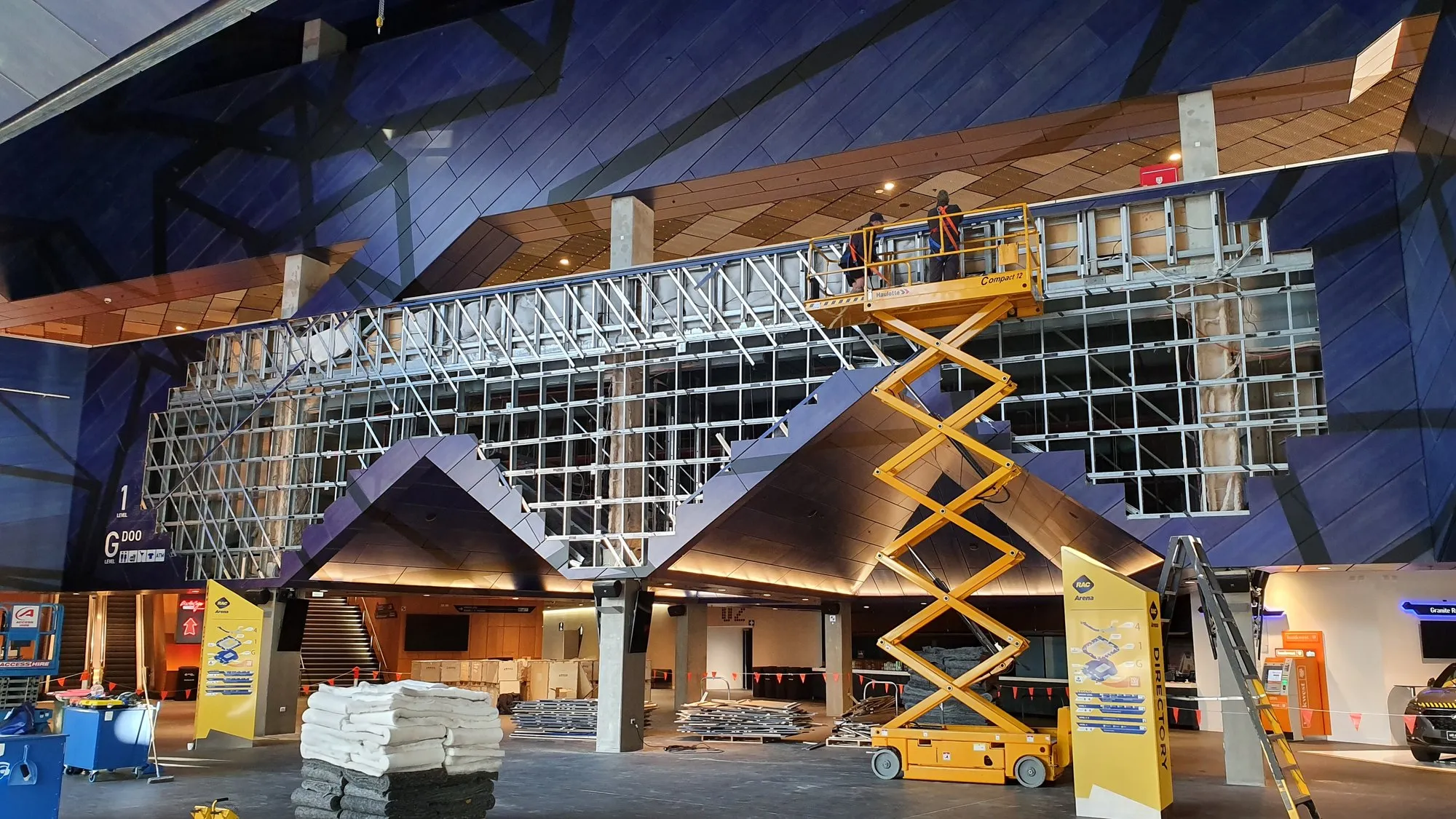 A steel diagrid frame with scissor lifts working on a large venue entrance screen